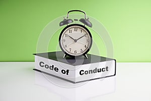 CODE OF CONDUCT text, Alarm Clock and book on green background.