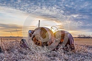 Coderre, SK- April 9, 2020: Sunburst at sunset over a vintage Case tractor abandoned in tall grass on the prairies in Saskatchewan