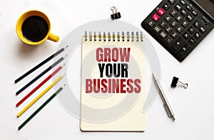 Cofee cup, calculator,notepad,pen and pencils on the white background. Business concept. Text GROW YOUR BUSINESS