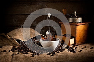 coffee art composition: scattered roasted beans from a bag, coffee grinder with ground coffee and a cup of coffee with a splash o