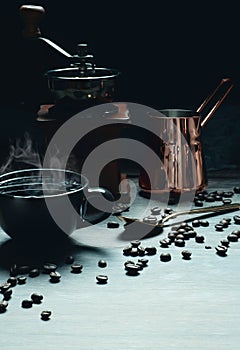 Coffee background of a cup of hot coffee on table with coffee grinder and coffee jar and roasted coffee beans in dark dimming