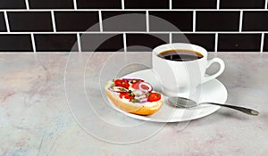 Coffee and bagel on white on pink tinged countertop with black subway tile background