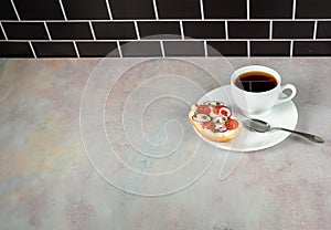 Coffee and bagel on white on pink tinged countertop with black subway tile background
