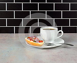 Coffee and bagel on white on pink tinged countertop with black subway tile background