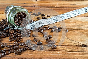 Coffee bean in glass bottle with tape measure on wooden background