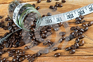 Coffee bean in glass bottle with tape measure on wooden background