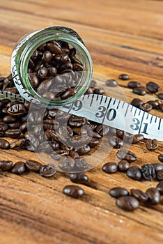 Coffee bean in glass bottle with tape measure on wooden background