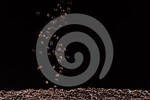 Coffee beans in the air flying in flight like a spray. On a black background, coffee shop advertising concept, copy space