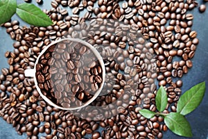 Coffee beans background with white cup in the middle and green leaves