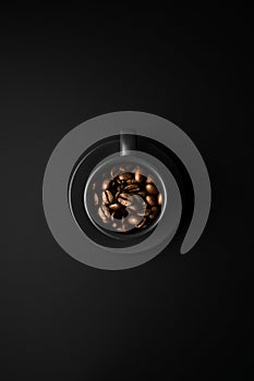 Coffee beans in black cup and saucer on a black surface.