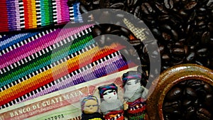 Coffee beans in burlap with mayan worry dolls and money on colorful indigenious handmade textiles. Concept for coffee