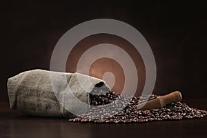 Coffee beans in burlap sack with scoop on brown background