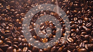 Coffee beans falling down on a a pile of smoking roasted coffee beans