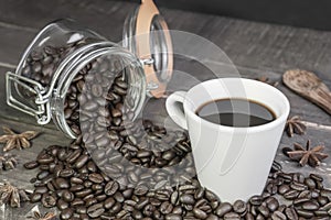 Coffee beans in glass jar with american black coffee cup on old wooden table.Concept of energy caffeine drink on rustic background