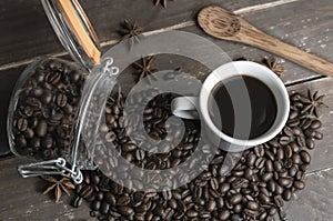 Coffee beans in glass jar with american black coffee cup on old wooden table.Creative cafe concept on rustic background
