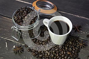 Coffee beans in glass jar with american black coffee cup on old wooden table.Creative cafe concept on rustic background