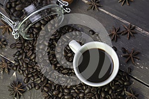 Coffee beans in glass jar with american black coffee in white cup on old wooden table.Top view of creative morning drink concept