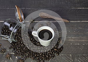 Coffee beans in glass jar with american black coffee cup on old wooden table.Top view of creative cafe concept on rustic