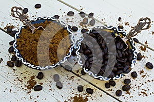 Coffee beans and grinded coffee in bowl on wooden white background.
