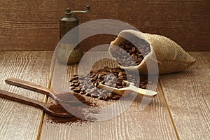 Coffee beans and ground coffee in wooden spoons on brown background. With old burlap bag and coffee grinder.