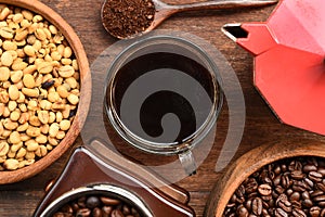 Coffee beans with ground coffee in wooden spoon and red kettle on the side