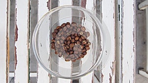 Coffee beans heap in glass heap on wooden table, top view