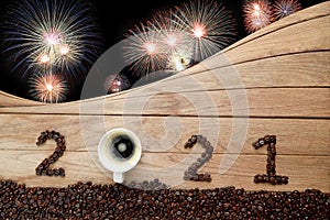 Coffee beans and hot fresh coffee in a white cup with foam and text 2021 for Happy New Year Concept. with fireworks background