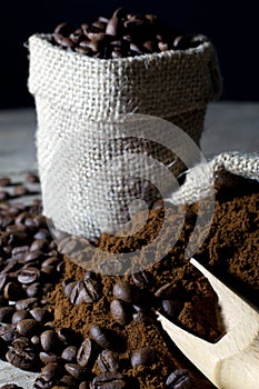Coffee Beans in Jute Bag and Ground Coffee with Wooden Scoop Closeup on Black