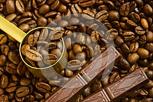 Coffee beans in a measuring spoon and chocolate on a background of freshly roasted coffee shallow depth of fiel