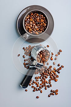 Coffee beans in mug and portafilter on gray background. Top view