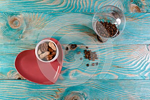 Coffee beans and nuts on a red plate in the form of a heart on a blue wooden background with perspective side view. Valentine`s d