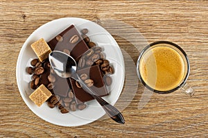Coffee beans, pieces of chocolate, sugar cubes, spoon in saucer, cup with coffee espresso on wooden table. Top view