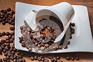 Coffee beans poured out of a cup with star anise on a saucer.