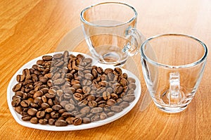 Coffee beans in saucer in heart shape, small transparent cups on wooden table
