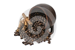 Coffee beans scattered from an inverted earthenware mug and a cinnamon stick on a white isolated background