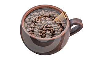 Coffee beans scattered from an inverted earthenware mug and a cinnamon stick on a white isolated background