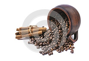 Coffee beans scattered from an inverted earthenware mug and a cinnamon stick on a white isolated background