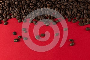 Coffee beans are scattered on a red paper background close-up, commercial copy space