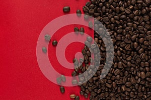 Coffee beans are scattered on a red paper background close-up, commercial copy space