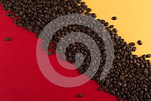 Coffee beans are scattered on a red and yellow paper background close-up, concept, commercial copy space