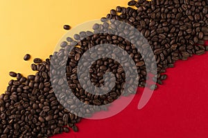 Coffee beans are scattered on a red and yellow paper background close-up, concept, commercial copy space