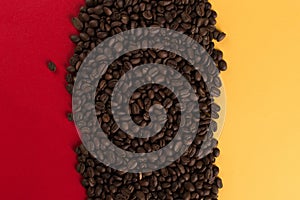 Coffee beans are scattered on a red and yellow paper background close-up, concept, commercial copy space