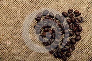 Coffee beans in the shape of a heart on a napkin of natural burlap background.