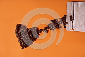 Coffee beans in the shape of a heart on an orange background spill out from a package