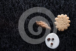 Coffee beans in spilled milk and brown sugar together with a cookie on a black background with silver lining.