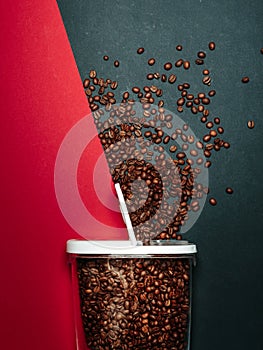 Coffee beans spilled out of jar on grey and red background