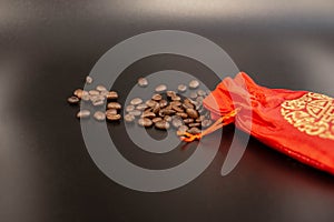 Coffee beans spilled from a red silk bag close-up with black background