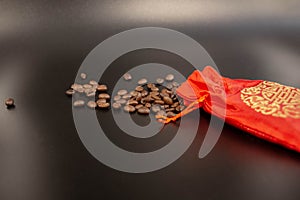 Coffee beans spilled from a red silk bag close-up with black background