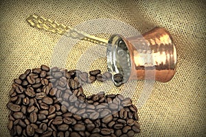 Coffee beans spilled from traditional Turkish copper coffee pot on a burlap