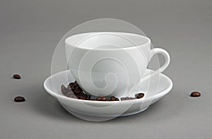 Coffee beans spilling out from a coffee cup on gray background.